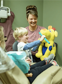 Dental assistant showing young boy how to brush his teeth with tooth brushing stuffed animal